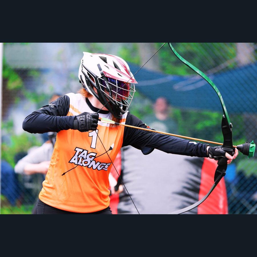 Trisha aiming during a combat archery match in a Tag Alongs jersey